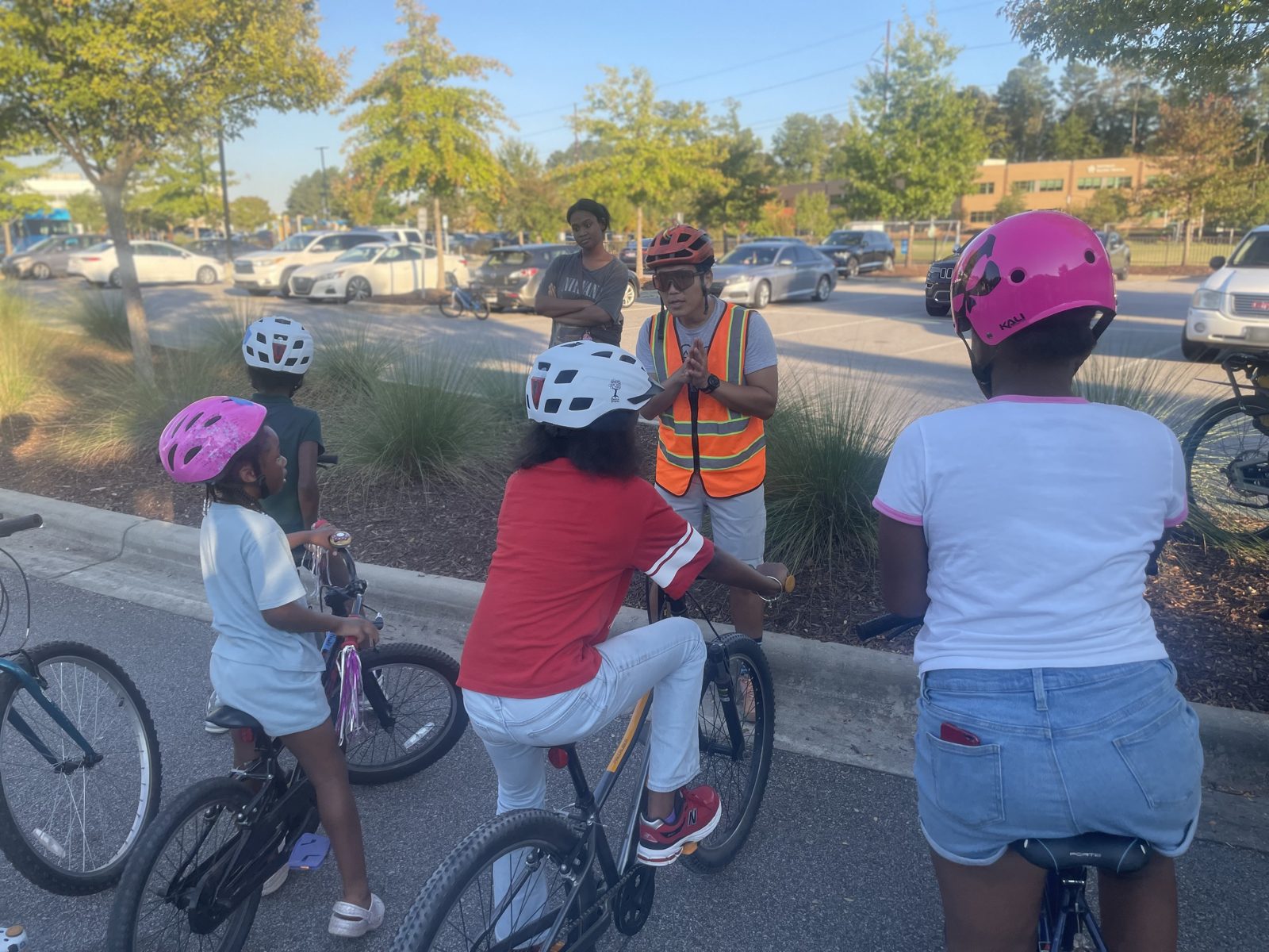 An instructor in an orange vest talks with a group of young riders