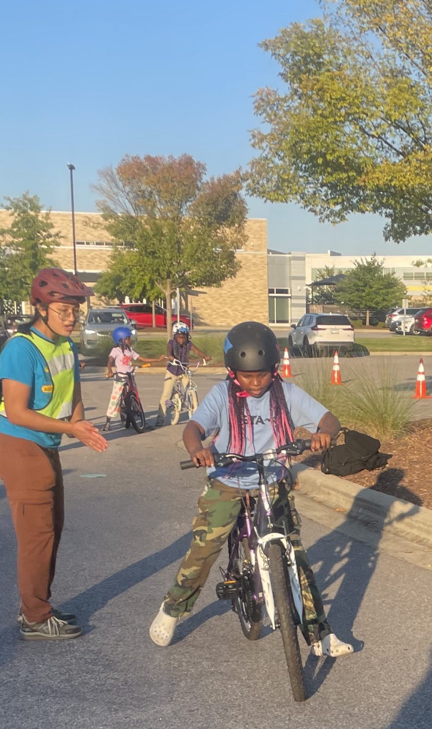 A young rider practices balancing while an instructor cheers her on